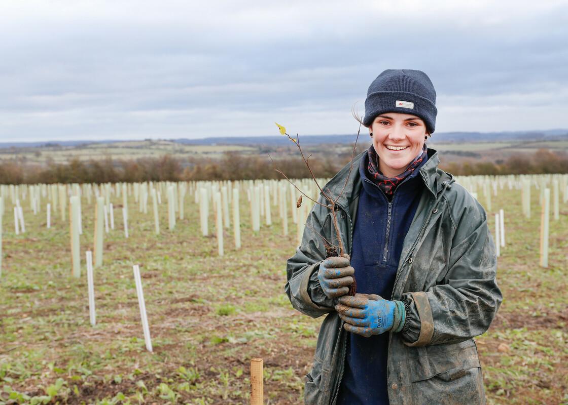 Forestry Intern (GRCF) Melissa stood smiling in a tree planting field holding a tree sapling
